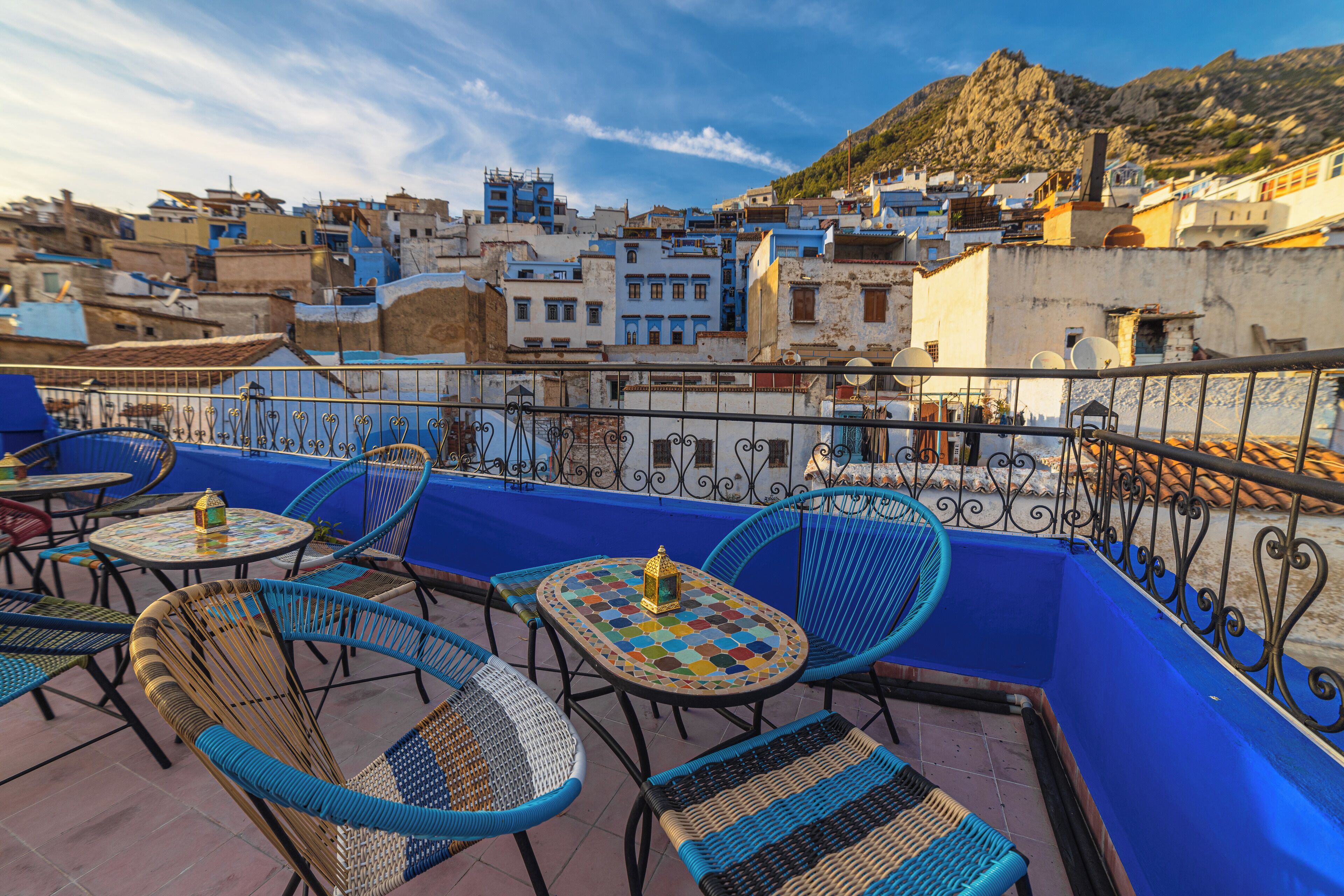 A terrace with blue railings, wicker chairs, and a tiled table with a lantern.