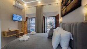 Ein modernes Hotelzimmer mit einem großen Bett, grauer Bettwäsche, einem Flachbildfernseher, einer Holzkammer und einem Bild an der Wand.