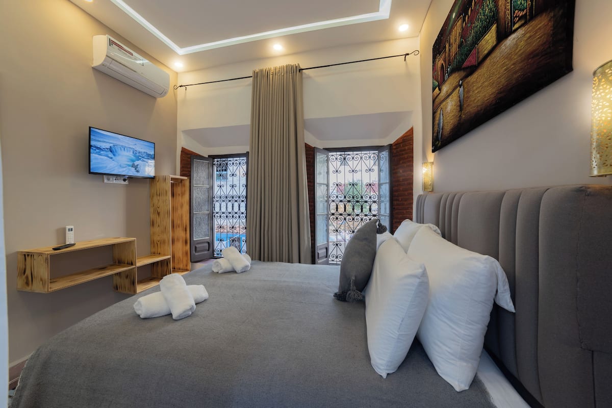 Une chambre d’hôtel moderne avec un grand lit, une literie grise, un téléviseur à écran plat, une étagère en bois et un tableau au mur.