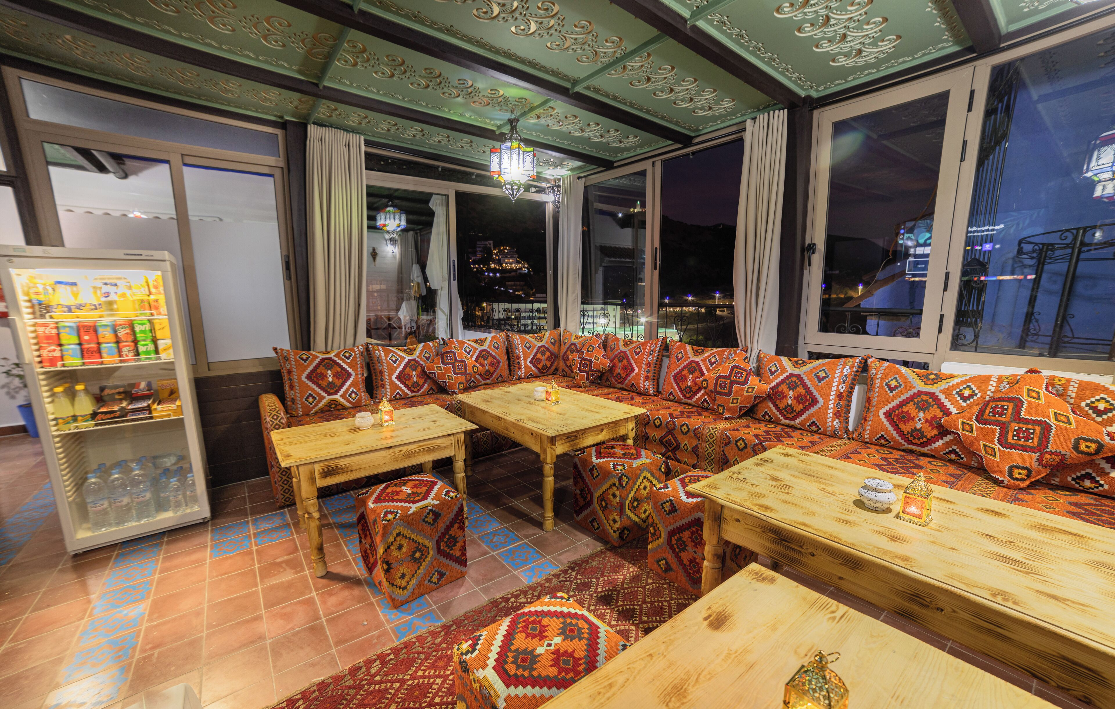 A cozy restaurant with a long wooden bench, small tables, and patterned cushions.