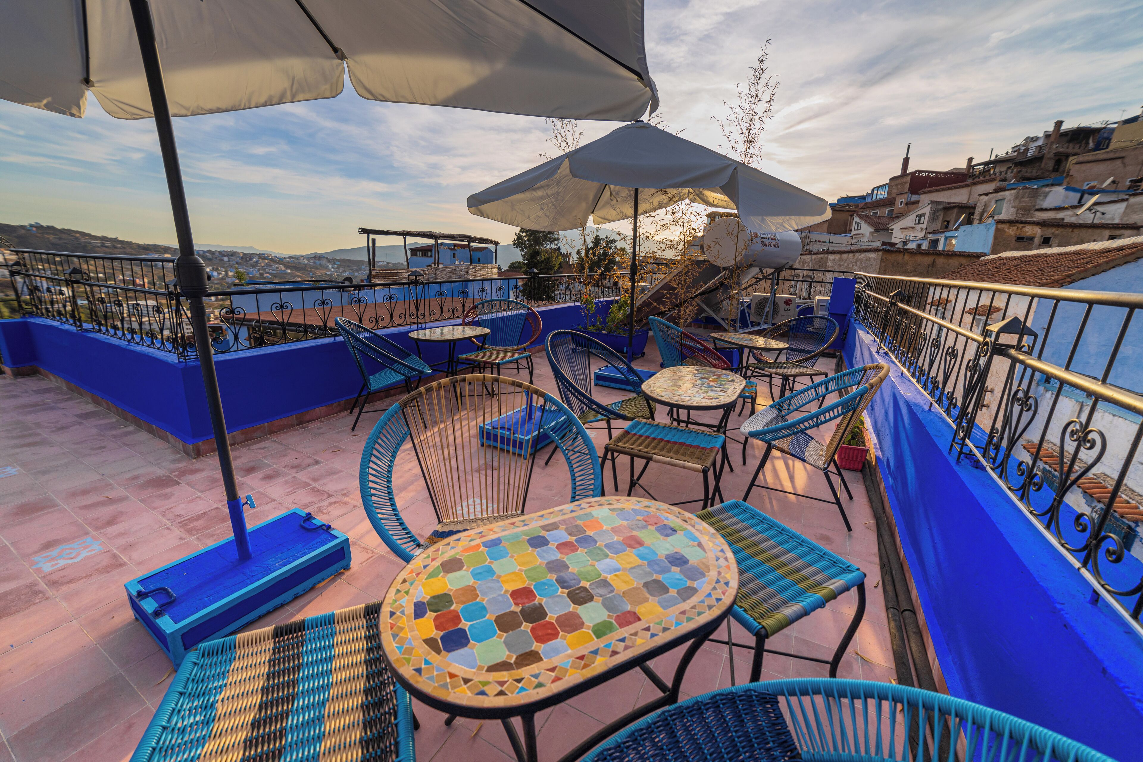 A rooftop terrace with blue railings, outdoor seating, and umbrellas.