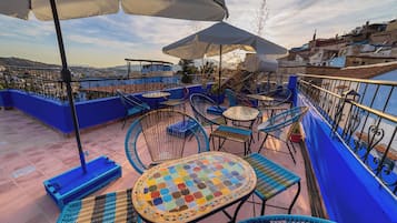 A rooftop terrace with blue railings, outdoor seating, and umbrellas.