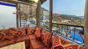 Ein Balkon mit Blick auf eine hügelige Landschaft, einem gemusterten Sofa und einem Metallgeländer.