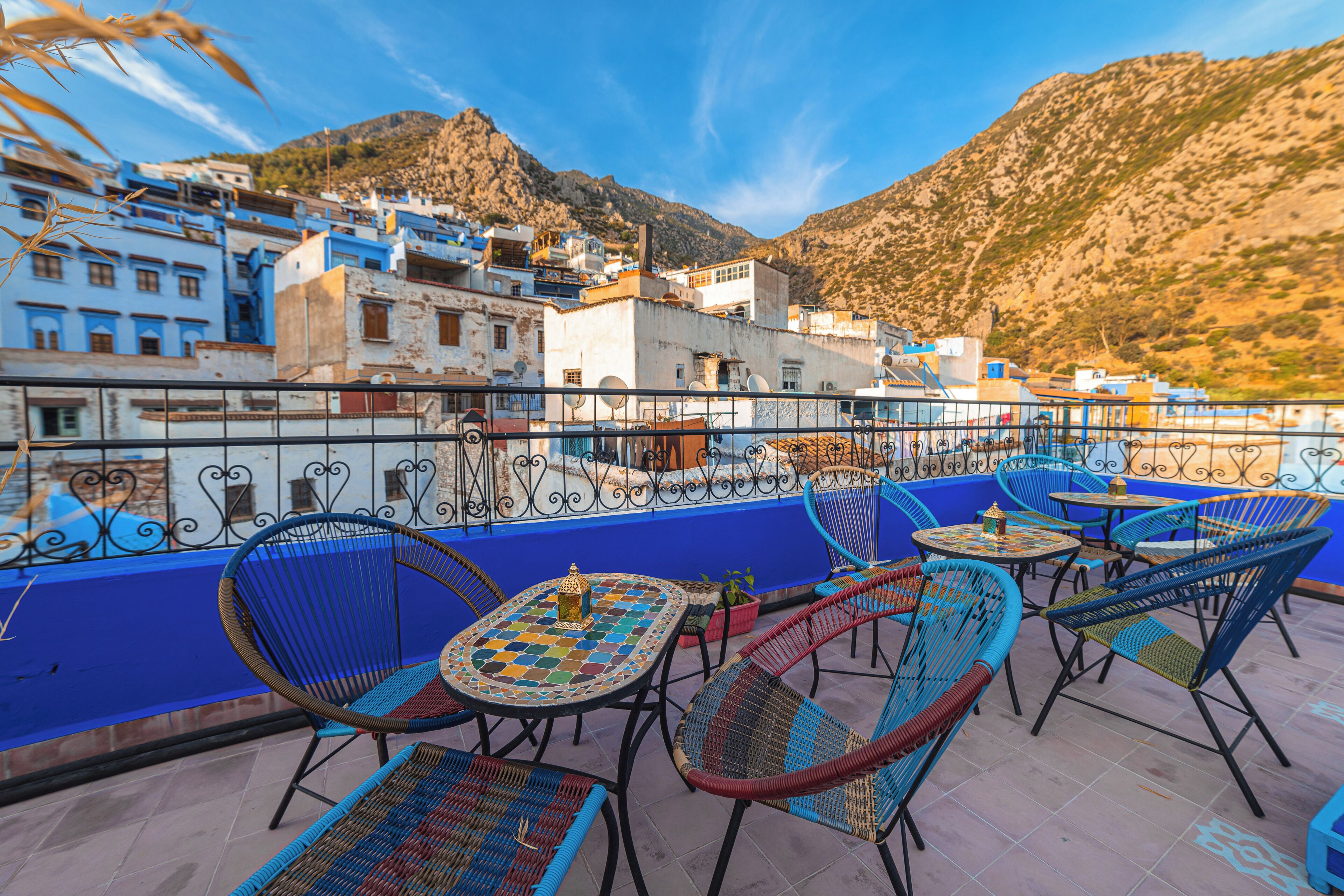 A terrace with outdoor seating, a view of a mountainous town, and a clear sky.