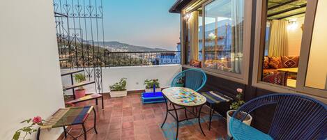 A balcony with a view of the city, two blue chairs, a small table, and potted plants.