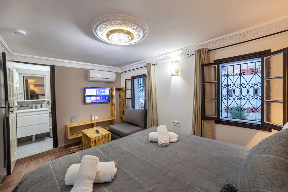 Une chambre d’hôtel comprenant un lit, une télévision, une petite table, un canapé et une fenêtre ornée d’une grille en fer décorative.