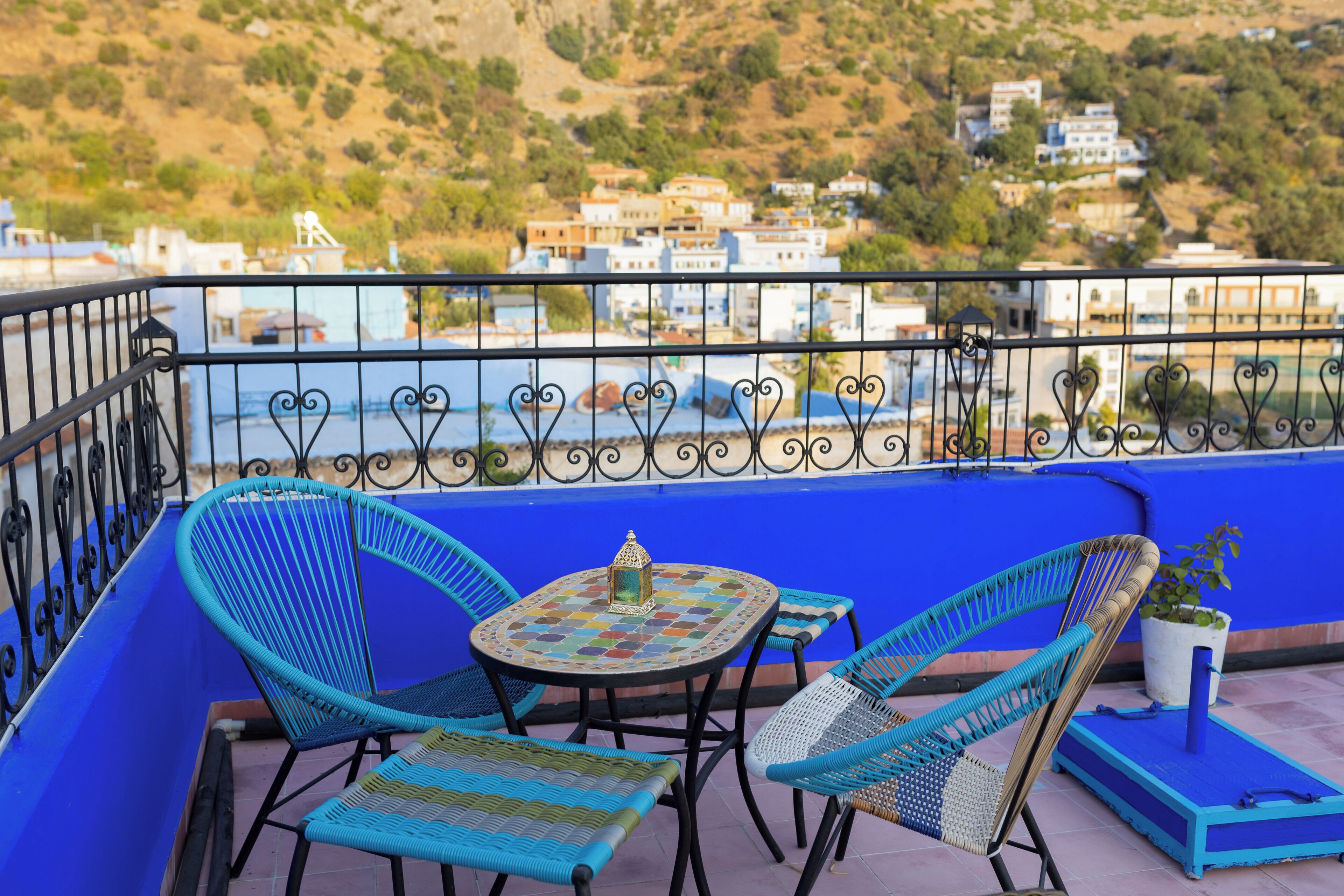 A balcony with blue walls, a small table with a decorative lantern, and wicker chairs.