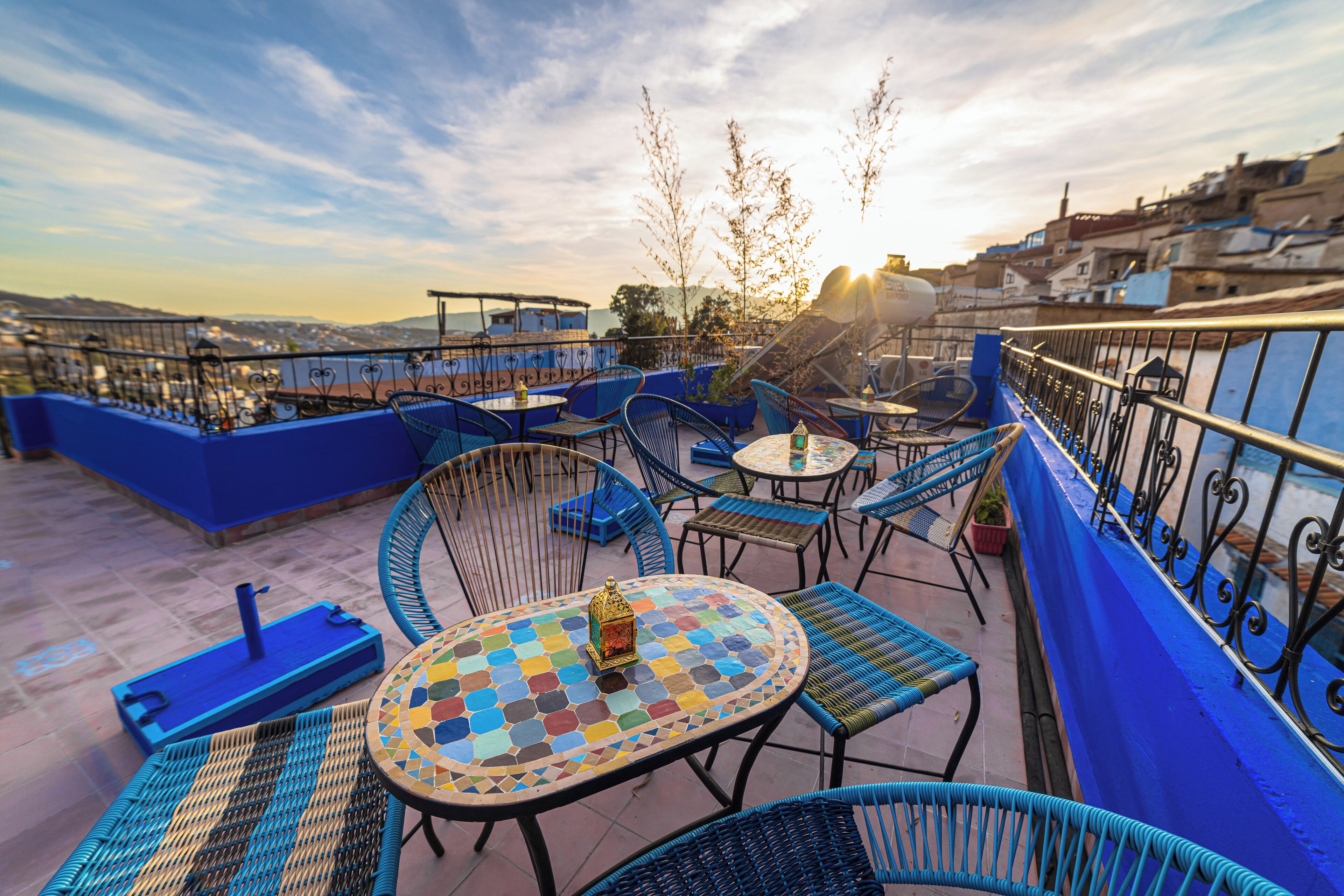 A rooftop terrace with blue railings, wicker furniture, and a mosaic table.