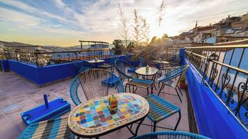 A rooftop terrace with blue railings, wicker furniture, and a mosaic table.