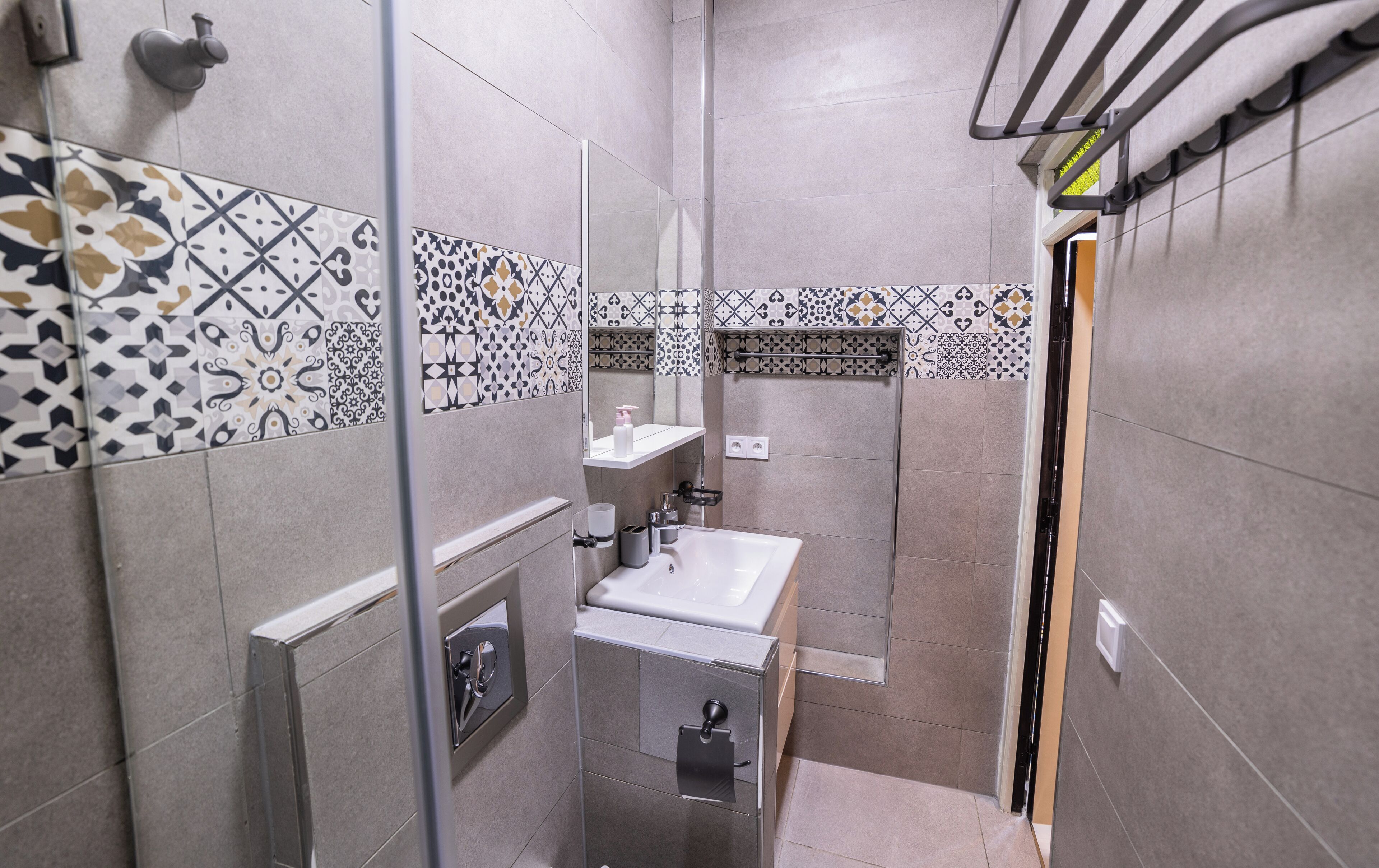 Een moderne badkamer met patroon betegelde vloeren, een glazen douchecabine, een wastafel en een toilet.