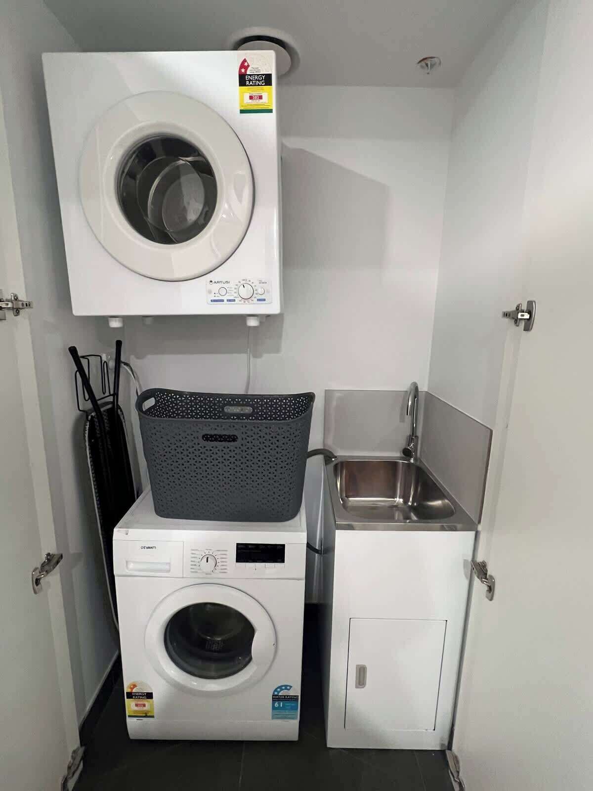 A compact laundry room with a front-loading washer and dryer, a small sink, and a drying rack.