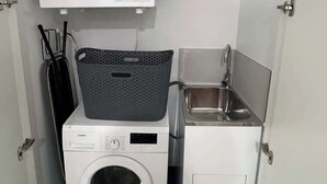 Un lavadero pequeño y funcional con lavadora y secadora de carga frontal, un lavamanos y un tendedero.