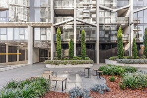 A modern building with a glass facade, outdoor seating area, and landscaped planters.