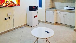 Eine kleine Küche mit Esstisch, Kühlschrank und einem an der Wand befestigten Fernseher.