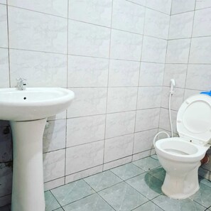 Et badeværelse med et hvidt håndvask og toilet, flisebeklædte vægge og grønne gulvfliser.