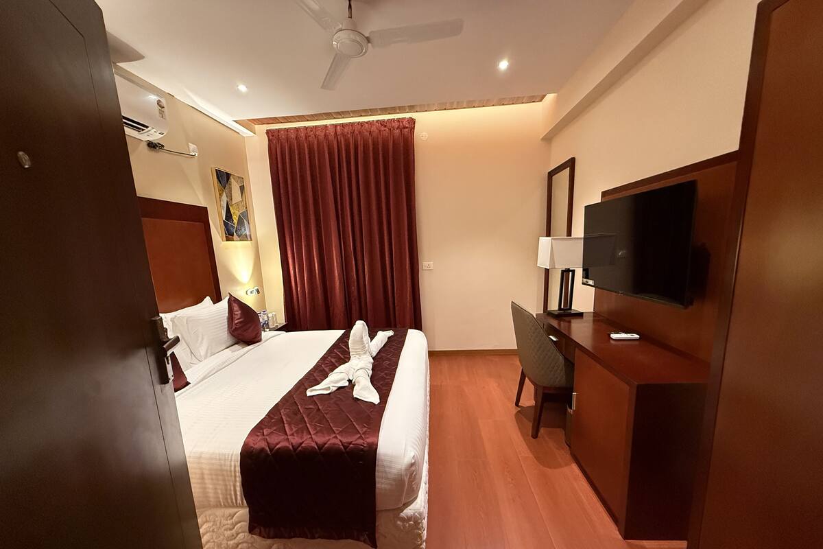 Een hotelkamer met een bed, een bureau, een televisie en een plafondventilator.
