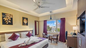 Quarto de hotel com cama, escrivaninha, cadeira, televisão e janela com cortinas.
