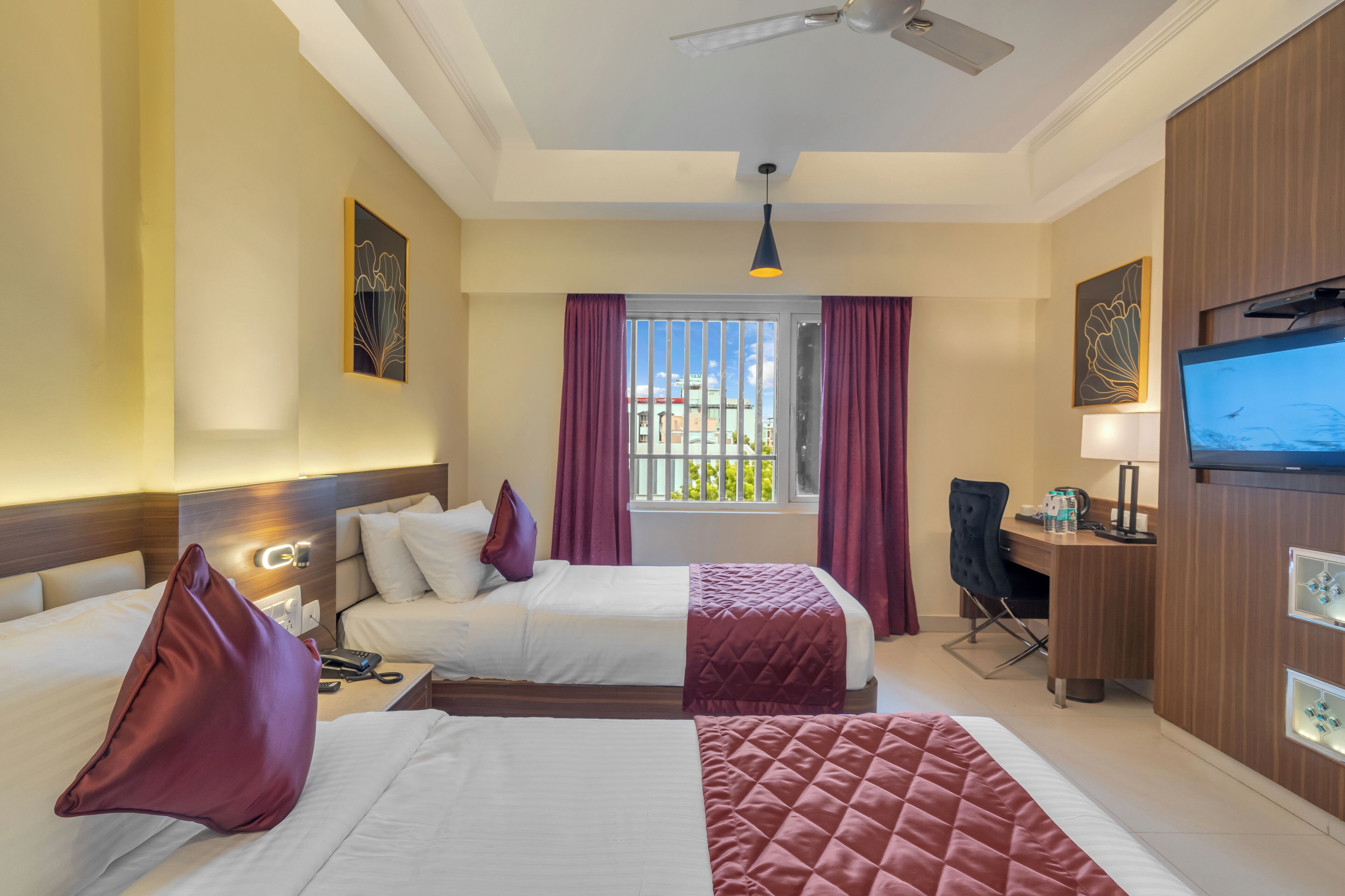A hotel room with two beds, a desk, a TV, and a window with curtains.