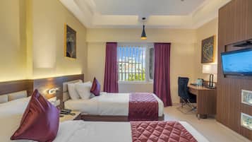 Habitación de hotel con dos camas, un escritorio, un televisor y una ventana con cortinas.