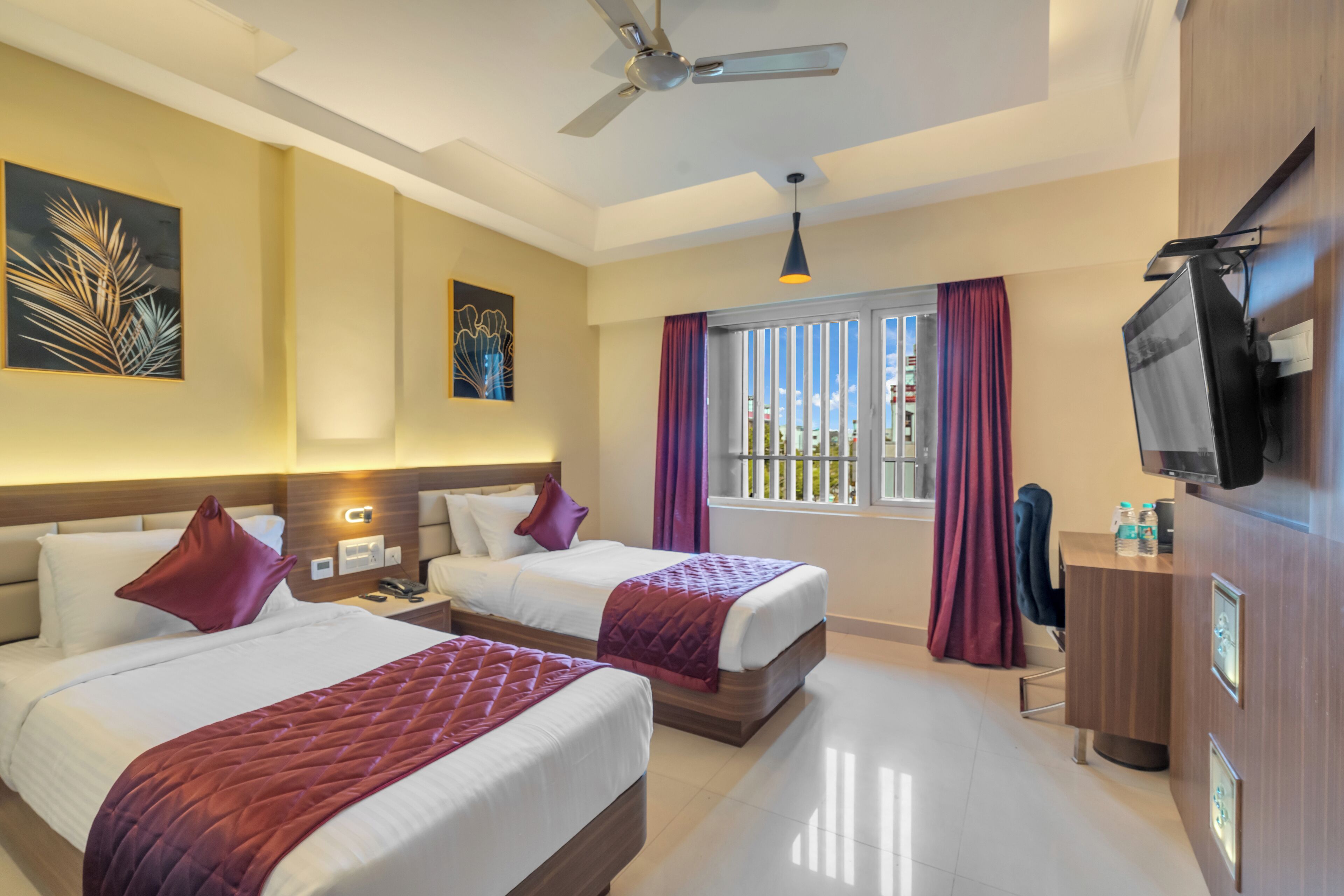 A hotel room with two beds, a desk, a TV, and a ceiling fan.