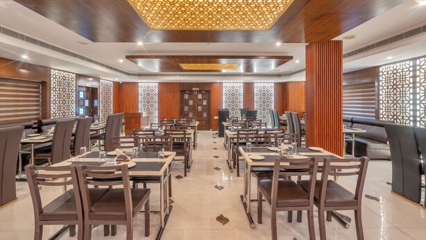 Uma sala de jantar ampla com várias mesas e cadeiras, painéis de madeira nas paredes e um lustre decorativo no teto.