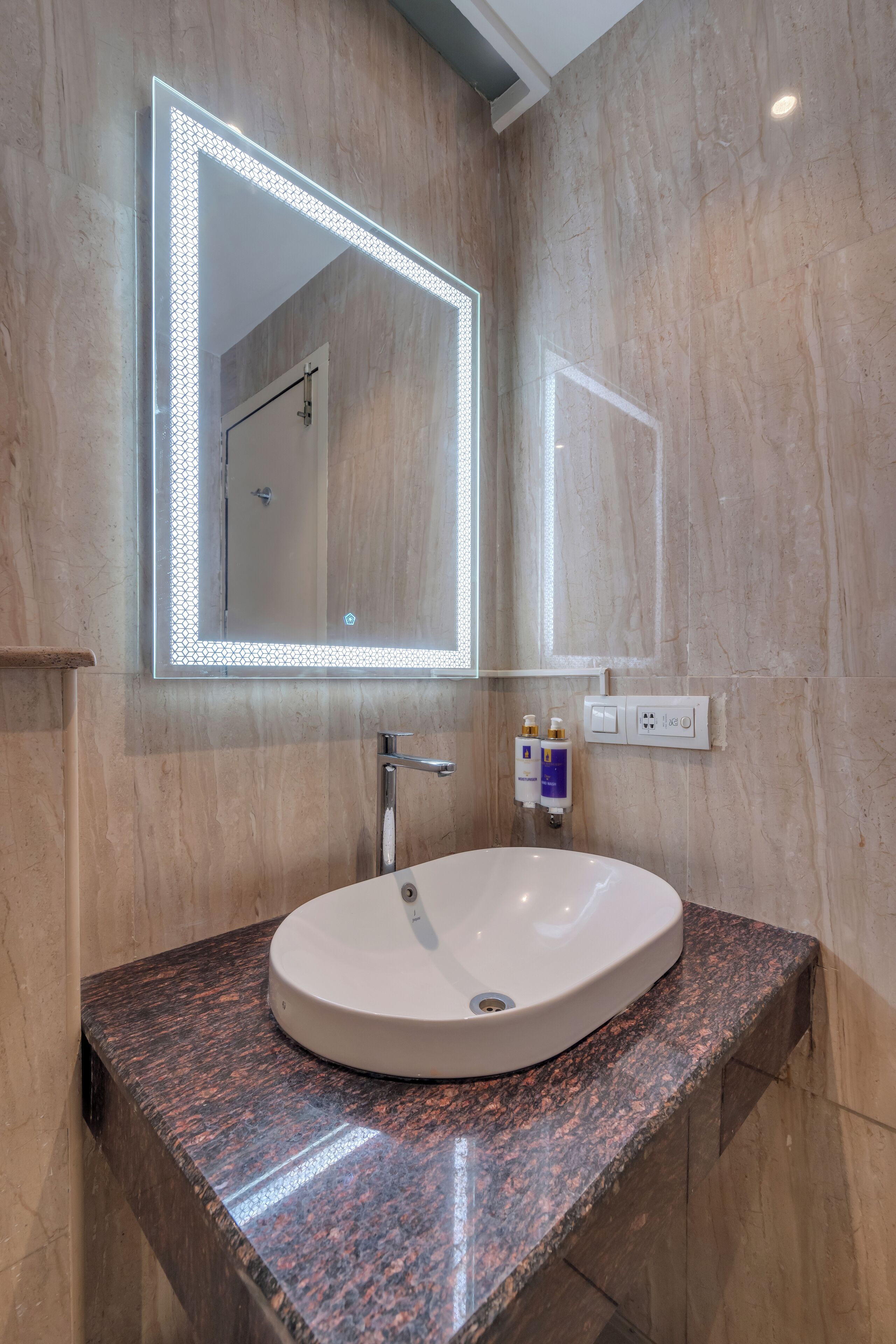 A bathroom with a round sink, a mirror with LED lights, and a marble wall.