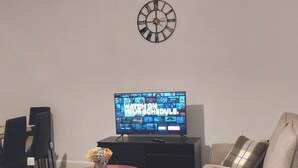 Una sala de estar con una televisión de pantalla plana, un reloj de pared y dos sofás.