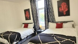 Doble habitación con dos camas, cortinas estampadas, una araña y un cuadro.