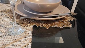 Una mesa de comedor dispuesta con dos fuentes, una copa de vino y cubiertos.