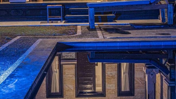 Ein formeller Außenbereich mit Pool, Stein-Säulen und einer Holzbank.