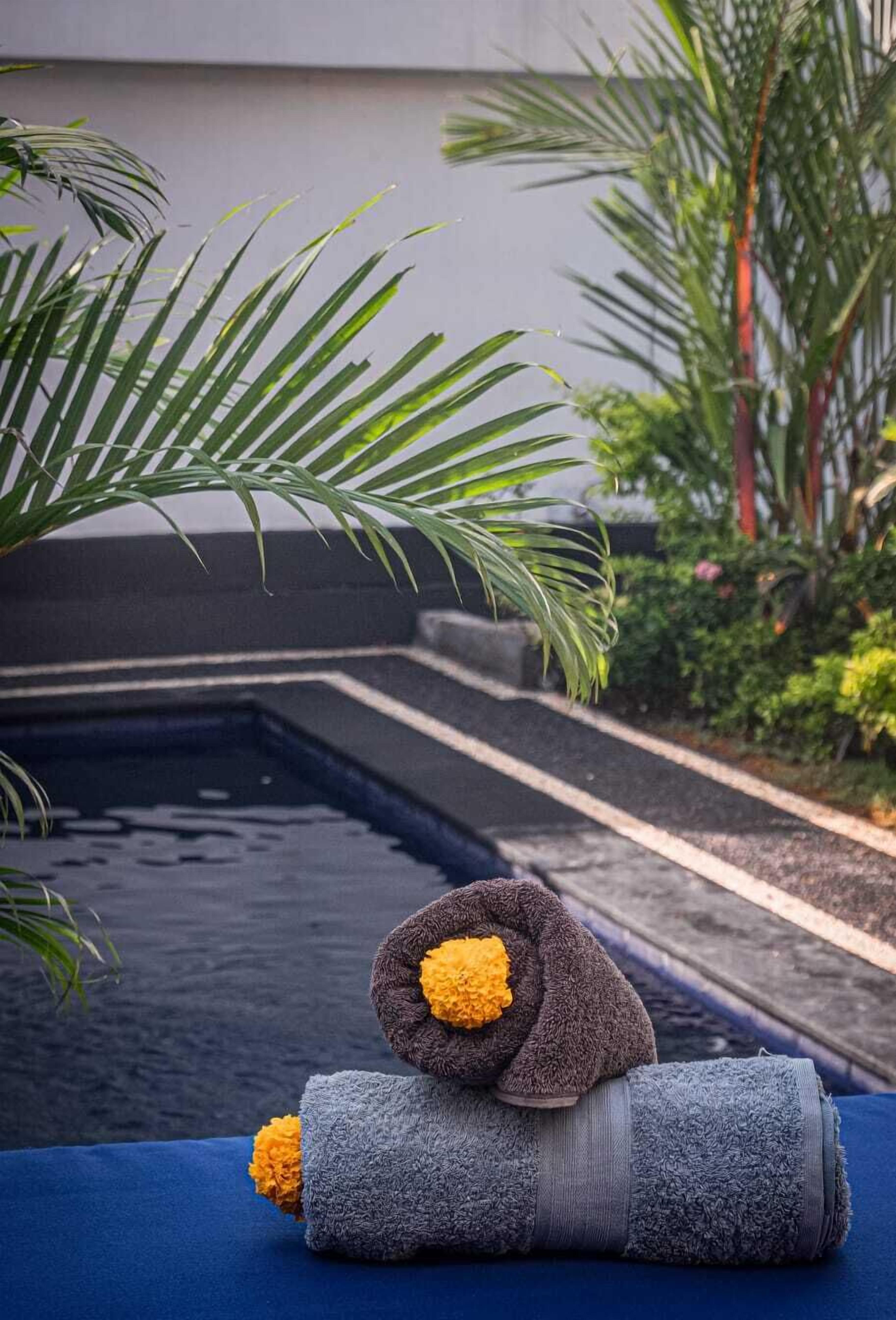 A pool area with a blue deck, a towel with a yellow flower, and a palm tree.