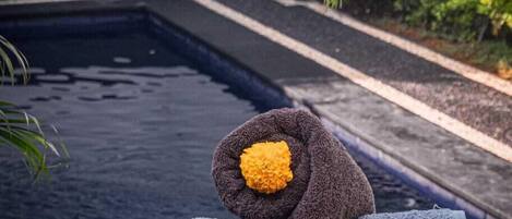 A pool area with a blue deck, a towel with a yellow flower, and a palm tree.