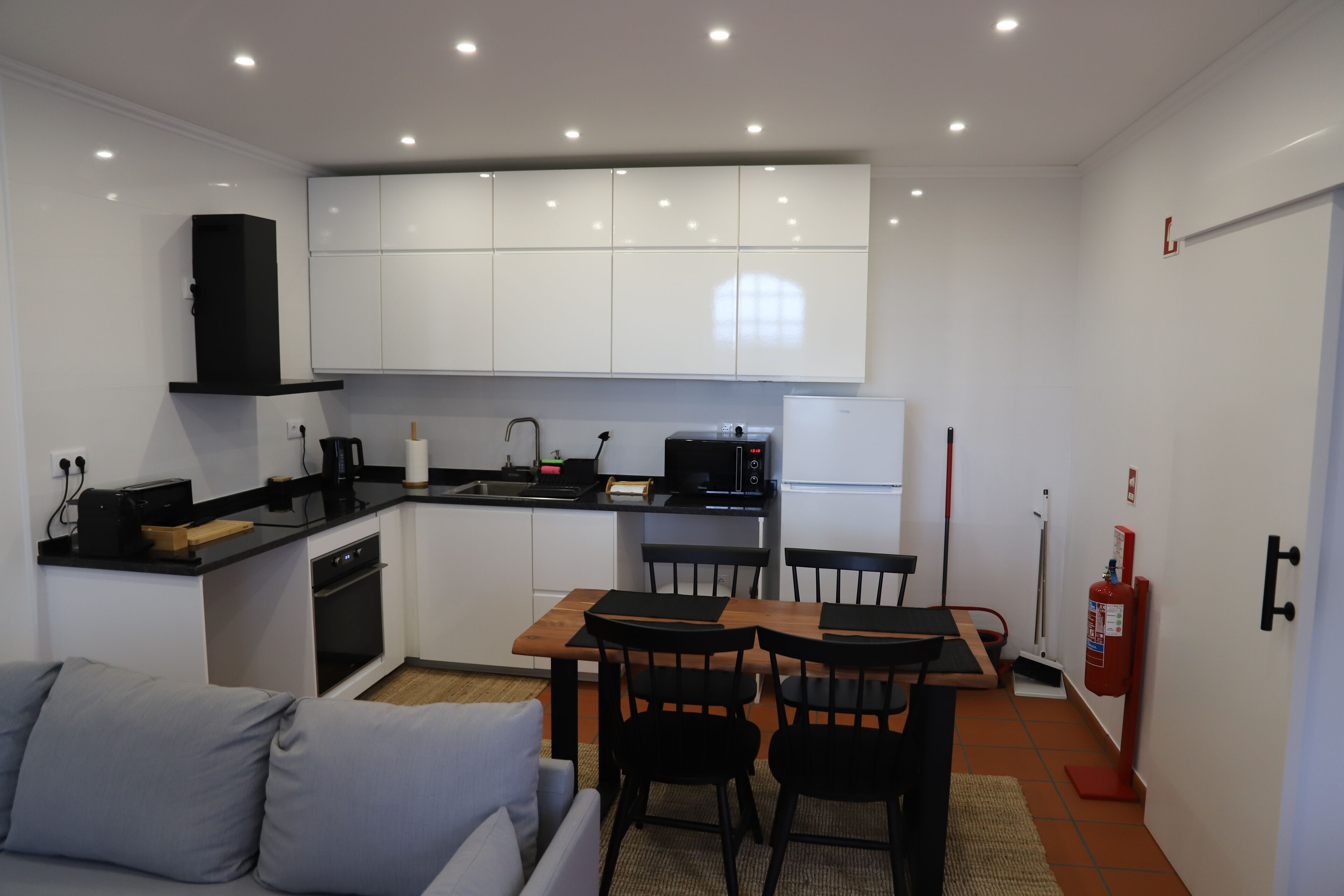 A compact kitchen with white cabinets, a black countertop, and a dining area with a table and chairs.