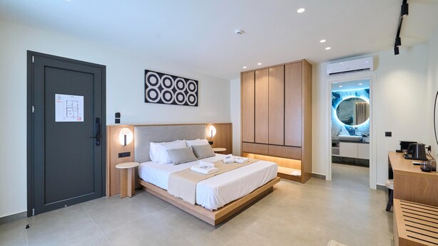 A modern bedroom with a large bed, bedside tables, a wardrobe, and a bathroom with a circular mirror. - Monarco Executive Rooms (Rhodes)
