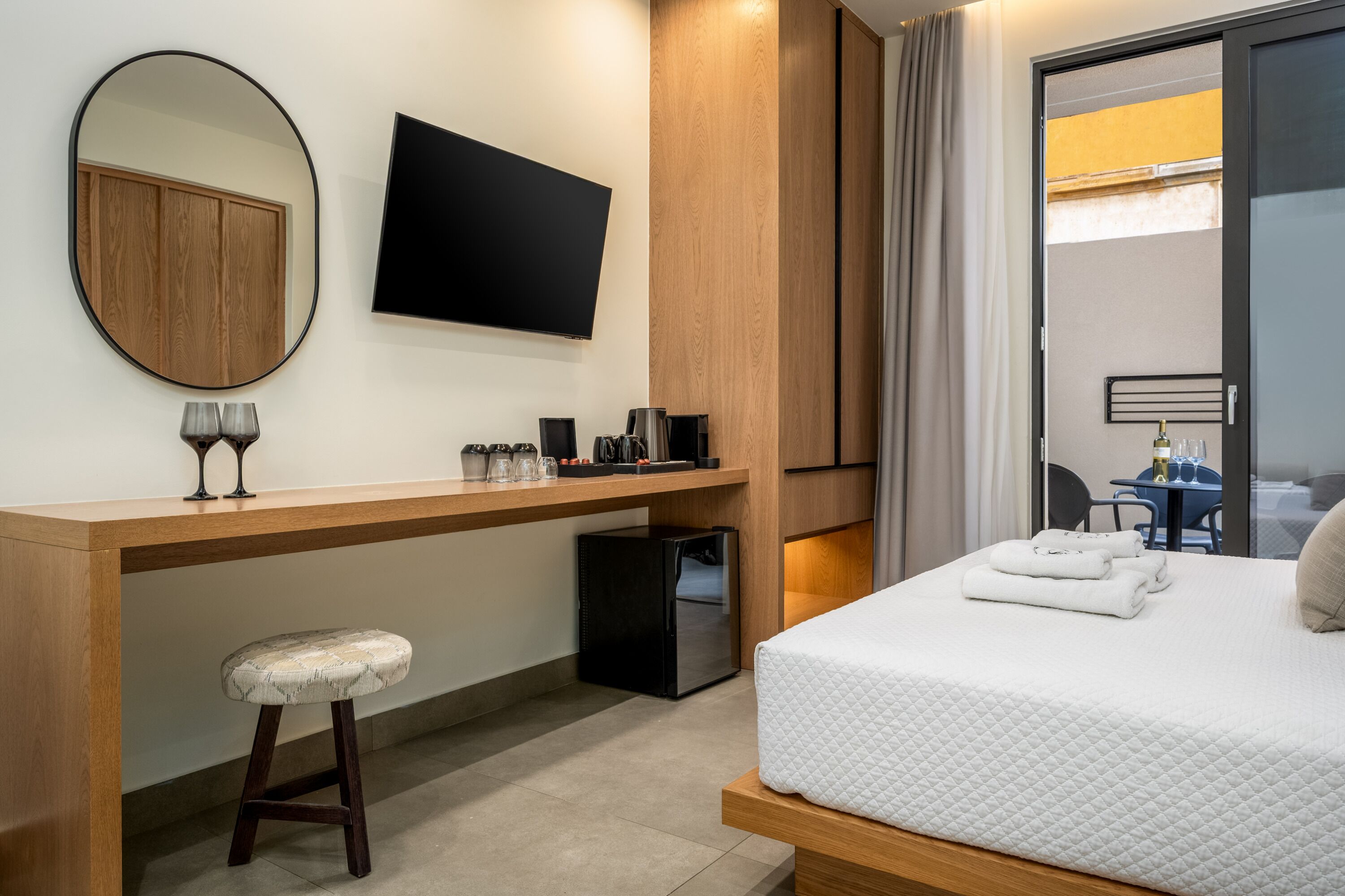 Een hotelkamer met een bed, een bureau met spiegel, een flatscreen televisie, een koffiezetapparaat en een klein krukje.