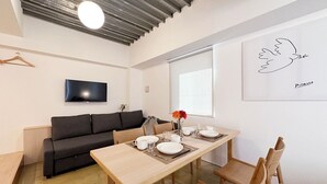 En moderne stue med sofa, spisebord, stole, et fladskærms-tv og et indrammet kunstværk på væggen.