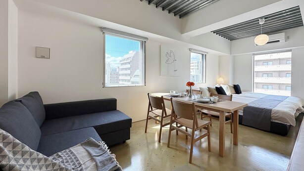 En moderne, lys lejlighed med spiseplads, sofa, seng og store vinduer med udsigt over byen.