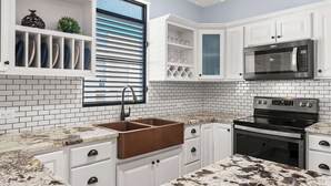 Une cuisine moderne avec des meubles blancs, un four à micro-ondes en acier inoxydable, un four et un plan de travail en granit.