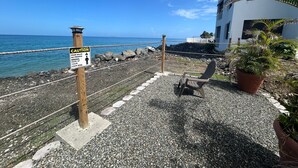 Une promenade en bord de mer avec un panneau d’avertissement, une chaise et un pot de fleurs.