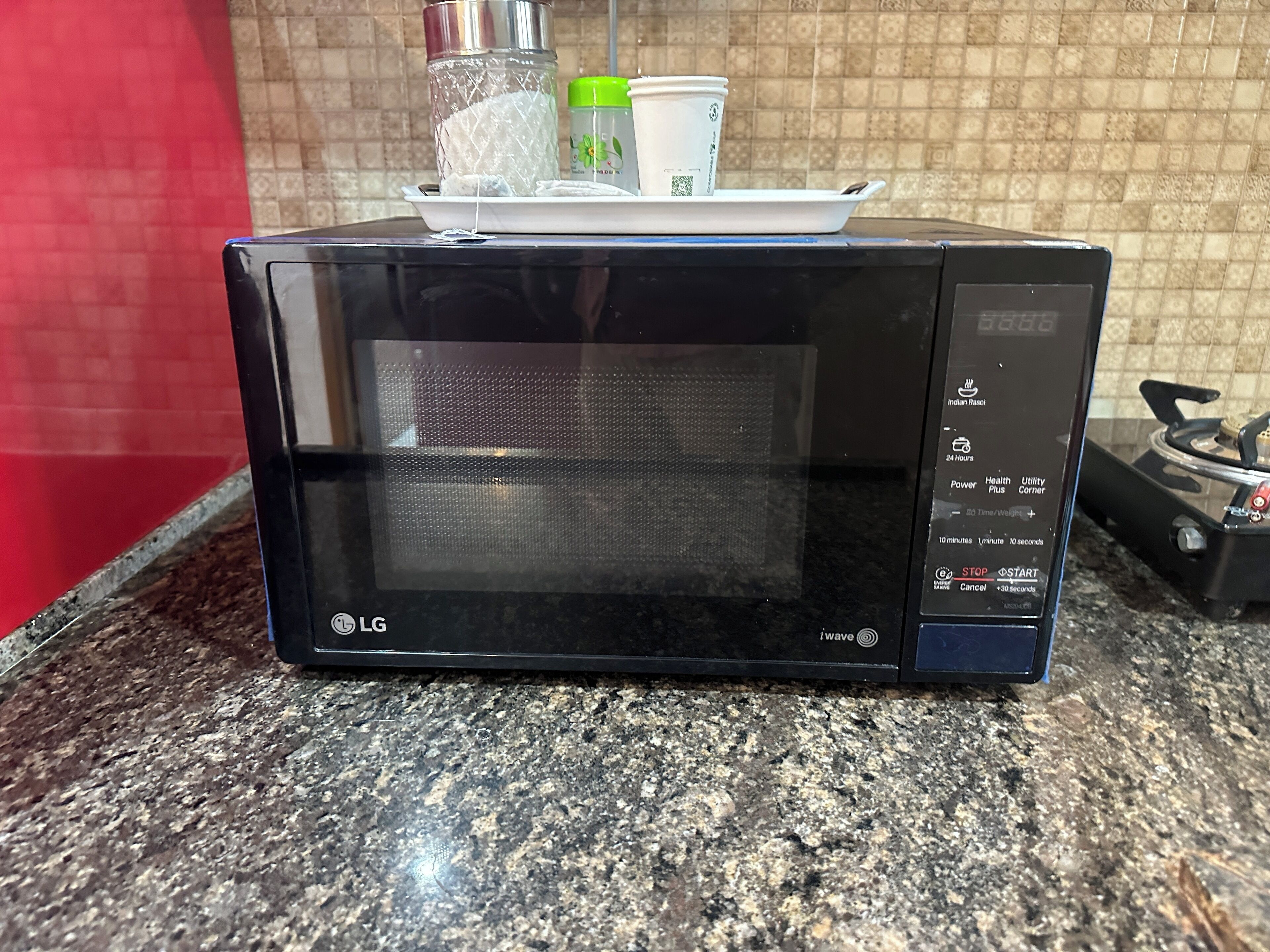 A black LG microwave on a granite countertop with a red wall in the background.