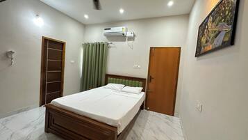 Un dormitorio con cama, ventilador de techo, aire acondicionado, una puerta y un cuadro en la pared.