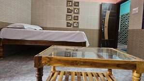 A room with a bed, a wooden table, a ceiling fan, and a wall-mounted air conditioner. - Swathi Rooms  (Tiruvannamalai)