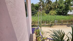 A building with a pink exterior, a tiled outdoor area with potted plants, and a view of a lush green landscape with trees and a clear sky. - Swathi Rooms  (Tiruvannamalai)