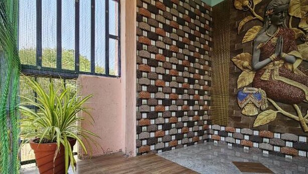 A room with a wooden floor, a brick wall with a mosaic, and a large window. - Swathi Rooms  (Tiruvannamalai)