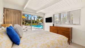 A bedroom with a bed, a wooden dresser, a TV, and a view of a swimming pool. - Luxury Palm Springs Estate 3Bedroom House & 3 Casitas, Salt Water Pool & HotTub (Palm Springs)