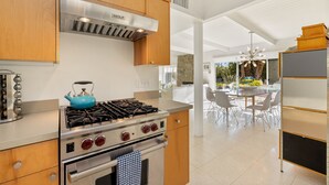 A modern kitchen with stainless steel appliances, wooden cabinets, and a dining area with a glass table and chairs. - Luxury Palm Springs Estate 3Bedroom House & 3 Casitas, Salt Water Pool & HotTub (Palm Springs)