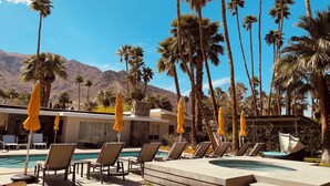 A pool area with lounge chairs and umbrellas, surrounded by palm trees and mountains. - Luxury Palm Springs Estate 3Bedroom House & 3 Casitas, Salt Water Pool & HotTub (Palm Springs)