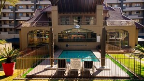A swimming pool area with a notice sign, surrounded by a fence, and a building with balconies in the background. - Hideout Hotel Apartment (Sandton)