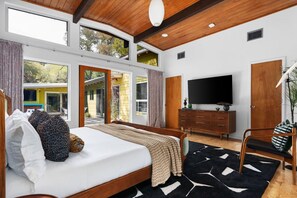 A bedroom with a bed, a TV, a dresser, and a large window. - MidMod Bungalow 5BR Heated Pool (Austin)