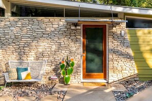 A stone facade with a wooden door, a bench with cushions, and a cactus plant. - MidMod Bungalow 5BR Heated Pool (Austin)